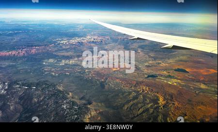 Ala di aeroplano sopra il colorato paesaggio desertico. Vista aerea dalla finestra di un aereo che mostra un'ala su terreni accidentati del deserto, mesa, canyon e largo Foto Stock