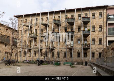Un edificio con facciata in pietra presenta una serie di balconi a sbalzo con ringhiere in metallo e piante in vaso, adagiati contro un cielo nuvoloso Foto Stock
