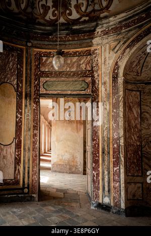 AGLIÈ, ITALIA – OTTOBRE 2025: Vista interna del castello di Agliè con pareti dipinte ornate, marmi invecchiati e porte che conducono a un corrido illuminato dal sole Foto Stock