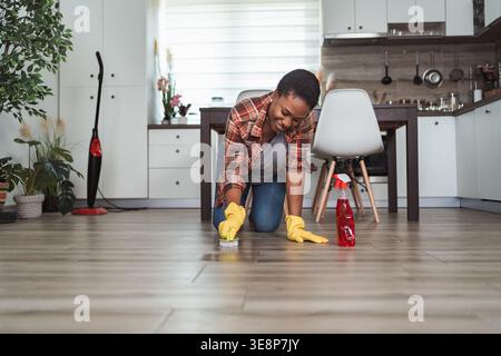 Giovane donna che strofina il pavimento della cucina godendosi il lavoro di casa indossando guanti gialli Foto Stock