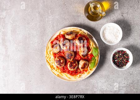 Un piatto di spaghetti classici conditi con polpette dorate e ricca salsa di pomodoro su un piatto di ceramica leggera. Foto Stock