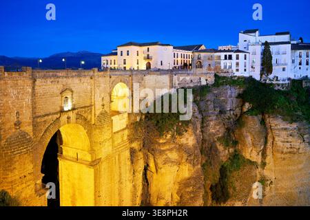 Ronda mostra il suo fascino di notte con edifici illuminati e la profonda gola di El Tajo. Il ponte collega i due lati della città. Foto Stock