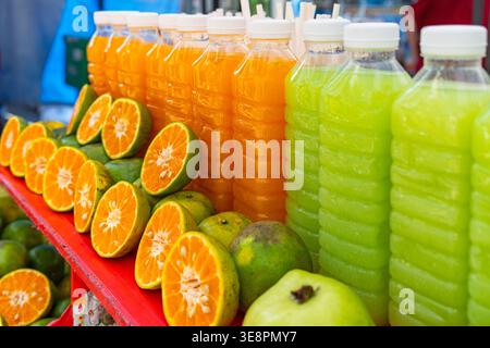 Succo di arancia e mela fresco in bottiglie di plastica al mercato di strada di Phuket, Thailandia. Luminose bevande tropicali con agrumi. Bevanda salutare Foto Stock