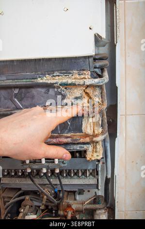 Il dito di un tecnico mette in evidenza un forte accumulo di minerali e ruggine sullo scambiatore di calore interno di un vecchio riscaldatore dell'acqua, indicando la necessità di una riparazione Foto Stock