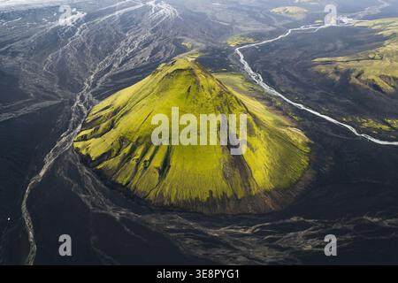 Vista aerea della vivace montagna Maelifell ricoperta di muschio verde, contrasta nettamente con le scure pianure di cenere vulcaniche, attraversate da un fiume glaciale Foto Stock