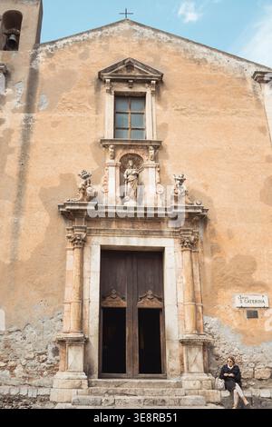 Vista della facciata intemprata di una chiesa storica con un campanile, una statua sopra la porta e una croce in cima, Taormina, Catania, Italia. Foto Stock