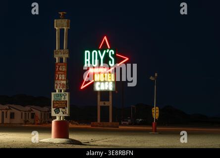 Amboy, Stati Uniti - 07 aprile 2026: La vista del Roy's Motel and Cafe si illumina contro il crepuscolo del deserto, proiettando un vibrante spettacolo al neon sopra l'histo Foto Stock