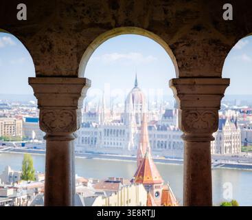 Il Parlamento di Budapest si vede attraverso l'arco del Bastione dei pescatori, iconico punto di riferimento ungherese, vista mozzafiato, architettura storica e la scena delle destinazioni di viaggio Foto Stock