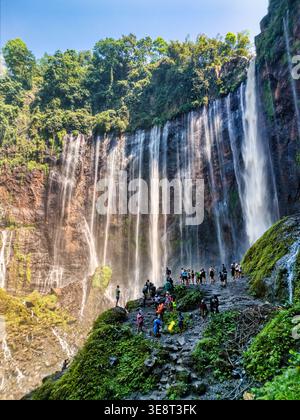 Vista aerea della cascata Tumpak Sewu con l'acqua che scende giù da lussureggianti scogliere verdi e persone riunite alla base di Kecamatan Pronojiwo, Jawa Timur, i Foto Stock