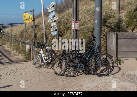 Blankenberge, Belgio - 5 aprile 2026: Biciclette parcheggiate vicino a un sentiero sabbioso con indicazioni stradali, dune costiere a Blankenberge. Notizie di viaggio, turismo Foto Stock