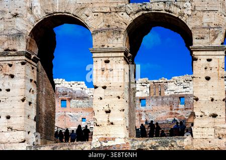 I turisti si stagliavano sotto gli archi del Colosseo a Roma, Lazio, Italia, con le pareti interne in travertino visibili. Foto Stock