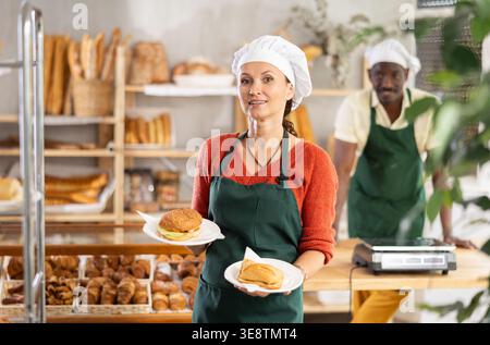 Imprenditrice donna, proprietaria di una panetteria, tiene in mano il panino in un piatto monouso Foto Stock