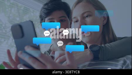 Messaggio in arrivo, due donne che si appoggiano, controllano le bolle della chat sullo smartphone a casa, con la parte superiore a righe Foto Stock
