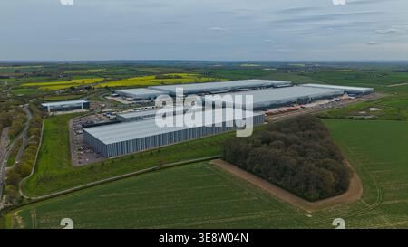 Vista aerea del parco industriale Appleby Magna con grandi magazzini moderni circondati da campi verdi e colza gialla sotto un coperto Foto Stock