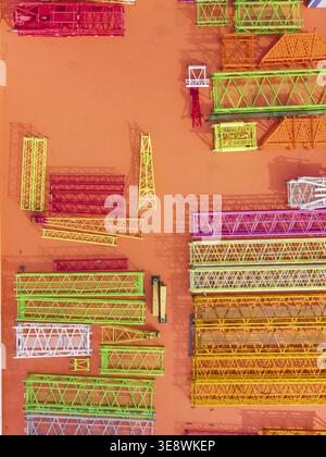 Vista aerea delle colorate sezioni reticolari della gru in verde, rosso e giallo disposte su una superficie industriale arancione a Taiwan. Foto Stock