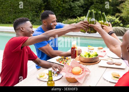 Quattro uomini che sbattono bottiglie di birra verde sul ponte che danno vita a etichette di cibo con le mani che brindano gli amici Foto Stock
