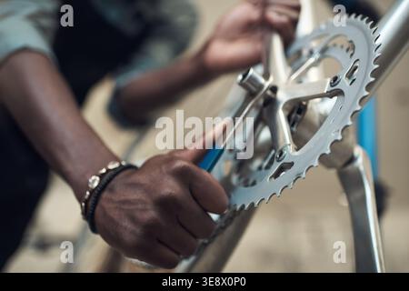 Bicicletta, ruota e mani con attrezzi in officina, manutenzione di catene o trasporti in piccole imprese. Meccanico, garage e persona con attrezzatura per Foto Stock