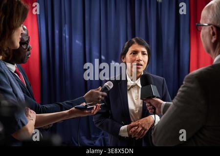 Un colpo medio di imprenditrice latina che risponde ai giornalisti durante la conferenza stampa, affrontando le domande dei media sulla politica pubblica e sulla leadership Foto Stock