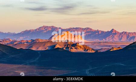 La luce del tramonto illumina il Monte Yanzhi oltre le scure creste del Monte Heidu a Qinghai, Cina. La prospettiva aerea cattura un contrasto straordinario. Foto Stock