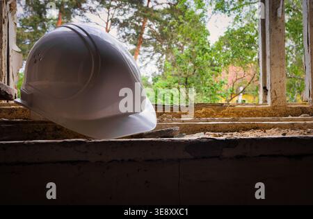 Elmetto bianco su macerie all'interno di un edificio crollato, simbolo di fallimento della costruzione, incidente industriale o degrado urbano Foto Stock