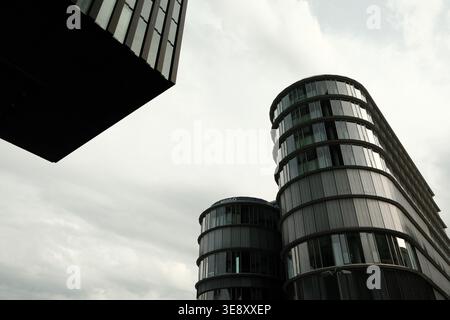 Una prospettiva ad angolo basso che guarda tra due moderni grattacieli di vetro verso un cielo coperto, con linee geometriche e riflessi. Foto Stock