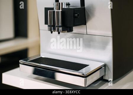 Vista ravvicinata della macchina da caffè automatica con finitura in metallo e doppio beccuccio sul bancone bianco. Elettrodomestici da cucina di lusso, macchina da caffè automatica Foto Stock