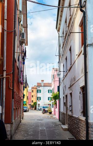 Vicolo stretto a Chioggia, Italia, caratterizzato da edifici vivaci e pensile per lavanderia, con un assaggio di più architettura alla fine della strada Foto Stock