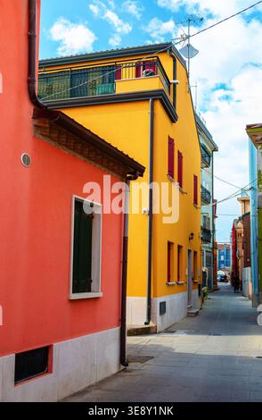 Stradina stretta di Chioggia, Italia, che presenta edifici colorati con facciate arancioni e gialle, creando una pittoresca scena urbana sotto un blu chiaro Foto Stock