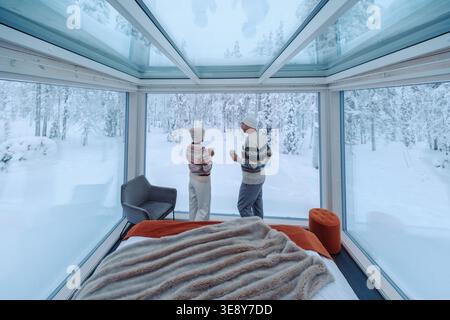 Due persone godono di viste mozzafiato da una lussuosa cabina di vetro ad Akaslompolo, Lapponia. Circondato da neve incontaminata, questo ambiente sereno invita al relax e all'avventura. Foto Stock