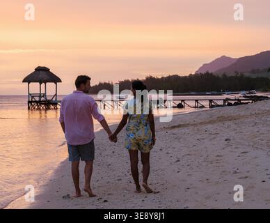 Una coppia cammina mano nella mano su una tranquilla spiaggia di Mauritius, circondata da splendidi colori del tramonto. L'atmosfera trasuda romanticismo, perfetto per una vacanza di lusso. Foto Stock