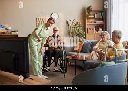 Ampia scelta di infermiere che assiste i residenti anziani durante l'attività di gruppo nella casa di cura, sostenendo l'assistenza quotidiana e l'impegno sociale Foto Stock