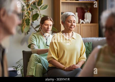 Donna anziana che riceve il check-up da una giovane infermiera adulta in una casa di cura, sostenendo l'assistenza agli anziani e la vita assistita Foto Stock
