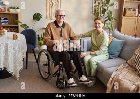Ritratto dell'anziano caucasico con disabilità seduto in sedia a rotelle accanto a una giovane infermiera adulta nella casa di cura Foto Stock