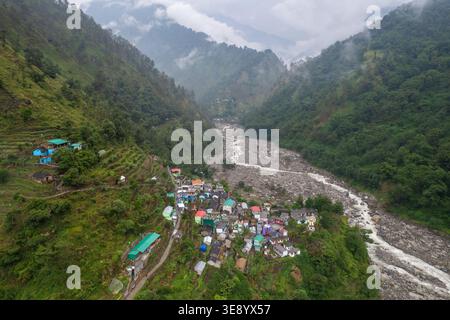 Una splendida vista aerea di un piccolo villaggio annidato in una valle circondata da montagne maestose e un fiume tortuoso, vicino al famoso Madhyamaheshwar te Foto Stock