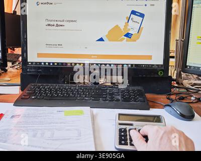 Kirov, Russia - 18 marzo 2026: Una persona lavora sulla pianificazione del budget utilizzando una calcolatrice, documenti finanziari e uno schermo del computer che mostra una paga online Foto Stock