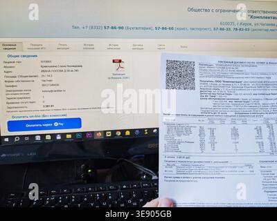 Kirov, Russia - 18 marzo 2026: La persona esamina le bollette e i documenti finanziari mentre lavora sulle spese mensili e sul budget a una scrivania con un Foto Stock