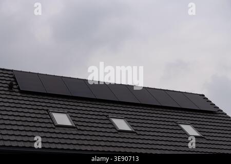 Moderni pannelli solari fotovoltaici installati su un tetto piastrellato scuro di una casa residenziale. Edificio ad alta efficienza energetica con tre finestre attico contro una Foto Stock