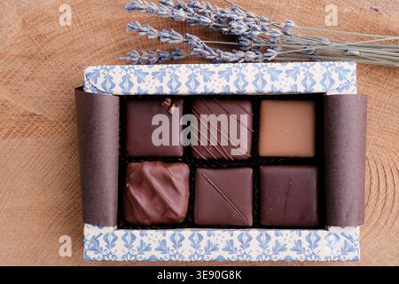 Varie praline di cioccolato in una scatola su una superficie di legno di quercia con lavanda secca. Cioccolato artigianale Bean to Bar. Cioccolato di qualità, marketing. Foto Stock