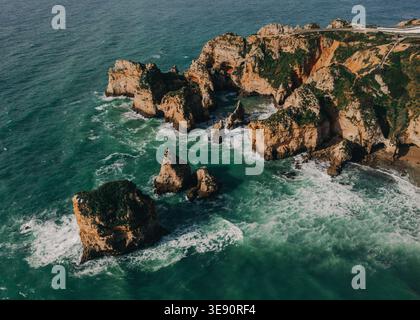 Vista aerea delle scogliere e delle scogliere rocciose circondate da acque turchesi con onde che si snodano intorno alle formazioni rocciose Foto Stock
