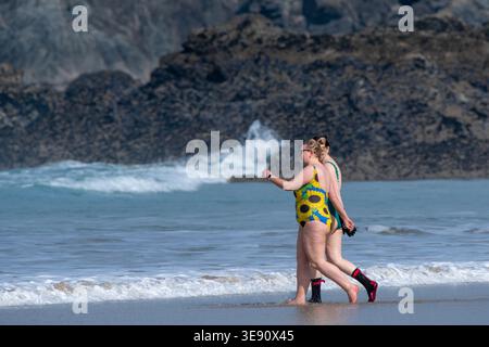 Two women walking to the sea on Fistral Beach for a cold water swimming session in Newquay in Cornwall in the UK. Foto Stock