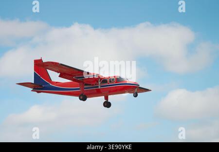 Un aereo rosso brillante che vola contro un cielo blu con nuvole morbide, catturato durante il volo Foto Stock