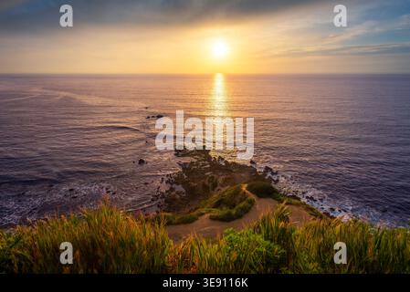 Tramonto dorato sulla costa rocciosa con un tranquillo orizzonte oceanico e una calda luce serale Foto Stock