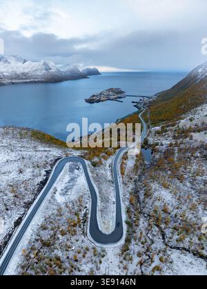 Vista aerea di una tortuosa strada di montagna con tornanti che si affaccia sul villaggio dell'isola di Husoy e sul fiordo sotto una leggera spolveratura di neve a Husoy Foto Stock