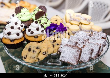 Un'invitante esposizione di dessert uruguaiani assortiti su un piatto di vetro, con cupcake, biscotti, brownie. Concentratevi su coccole, dolcetti e Foto Stock