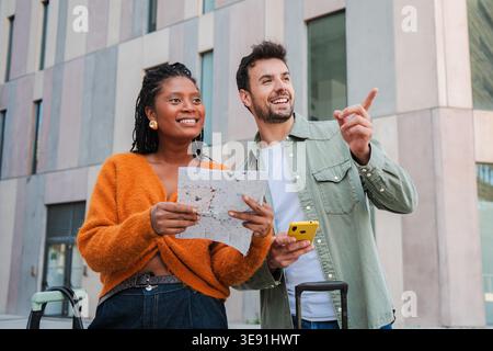 Felice ed entusiasta giovane coppia che scopre con gioia un nuovo luogo, navigando con sicurezza con una mappa e uno smartphone, godendosi la loro avventura Foto Stock