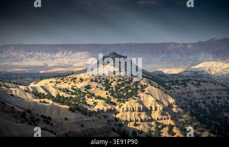 Colline e creste illuminate dal sole si estendono su un paesaggio aspro sotto un cielo spettacolare Foto Stock