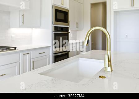 Primo piano di un lavandino in stile fattoria con rubinetto dorato in una cucina bianca luminosa. Foto Stock