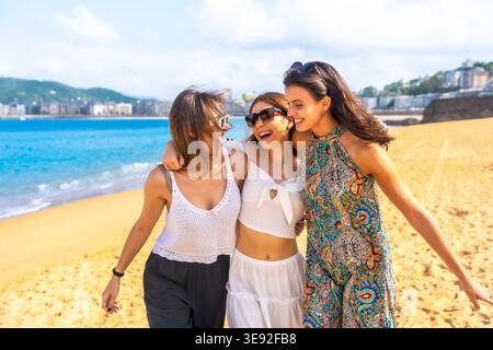 Tre giovani amiche che ridono camminando lungo la spiaggia Foto Stock