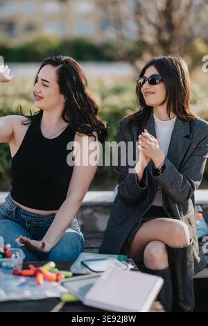 Due studentesse sorridenti e chiacchierate all'aperto sulla panchina del campus con i notebook Foto Stock