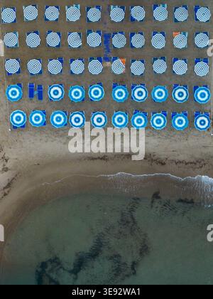 Vista aerea di file di ombrelloni e lettini a righe blu e bianche sulla spiaggia sabbiosa di Cefalù, Sicilia, Italia. Foto Stock